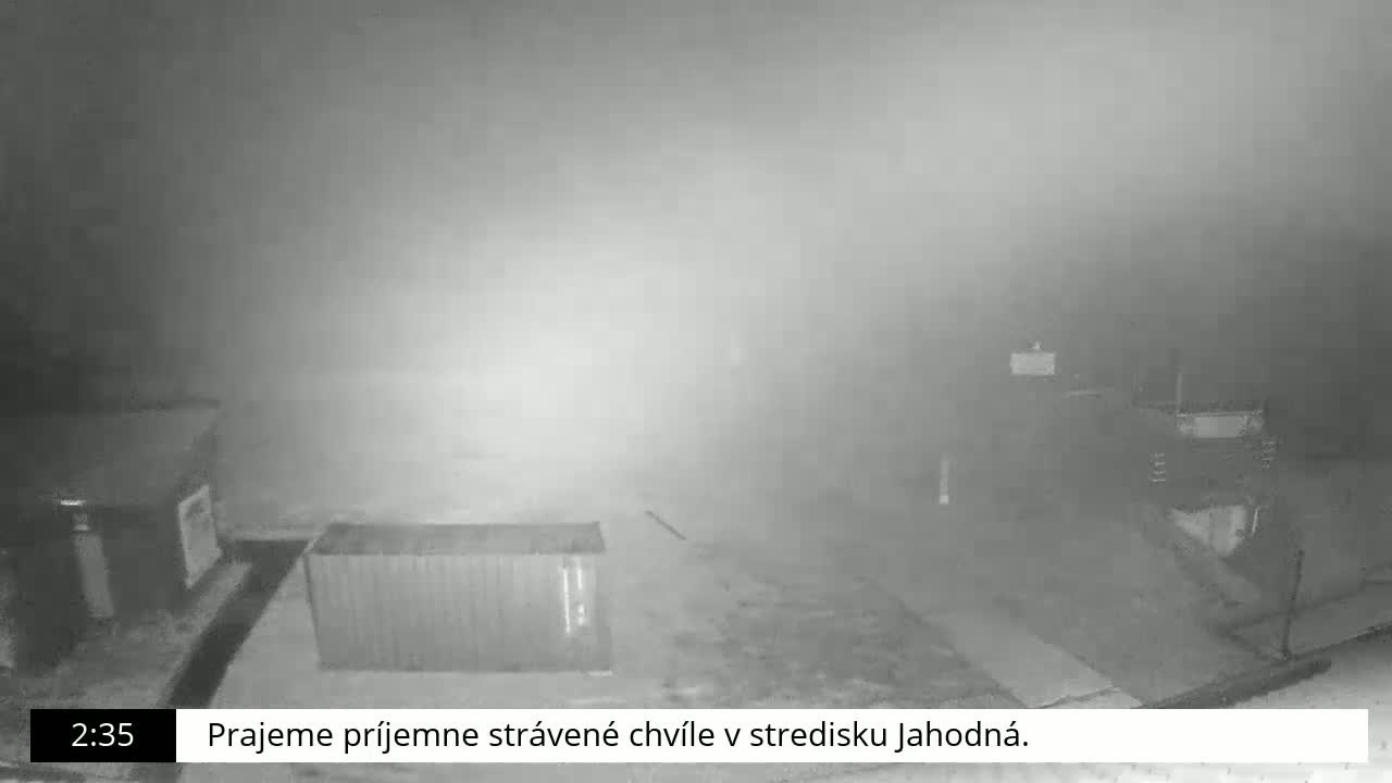 A nighttime, foggy scene shows a shipping container and several indistinct buildings.
