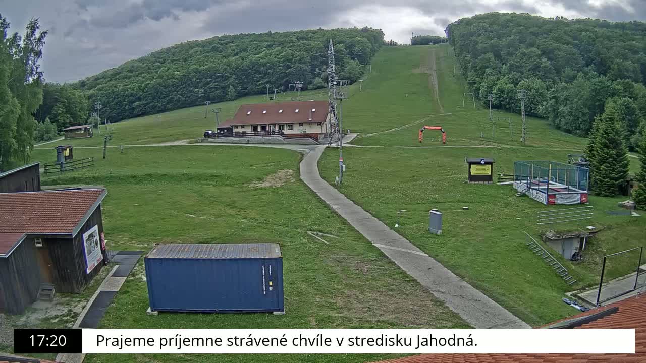 A grassy ski resort with a building, a paved path, and a cloudy sky is shown.