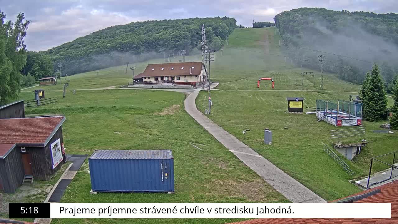 A grassy ski resort with a building, lift infrastructure, and a light fog covering the hillside.