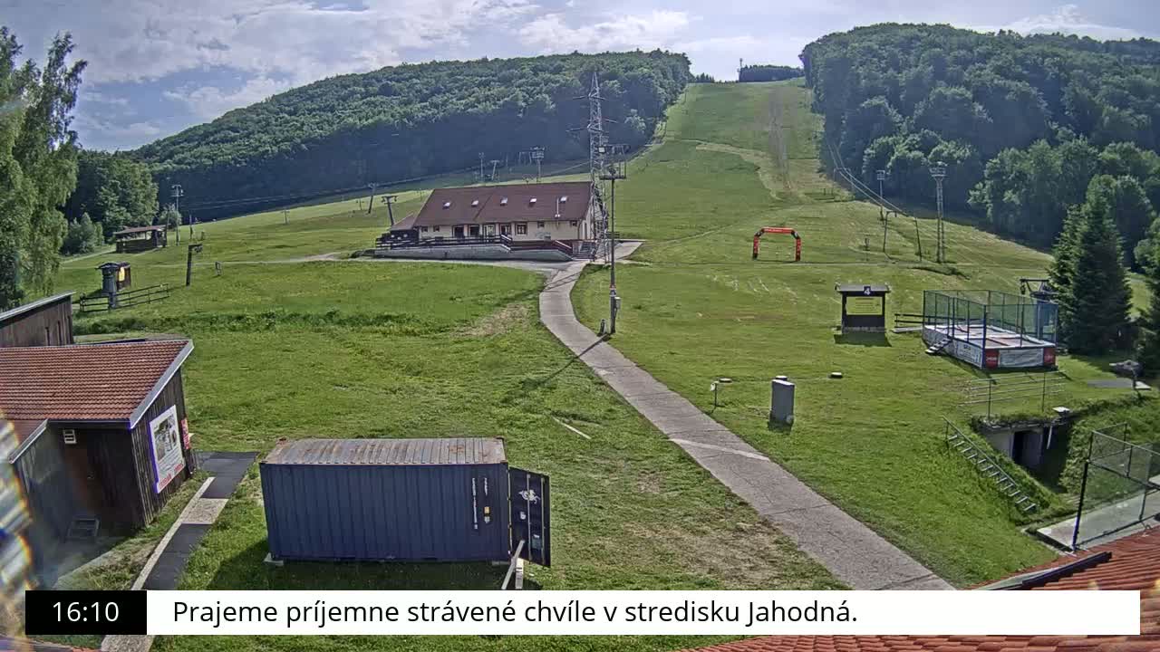 A grassy hillside with a ski lift, a building, and other structures is visible on a sunny day.