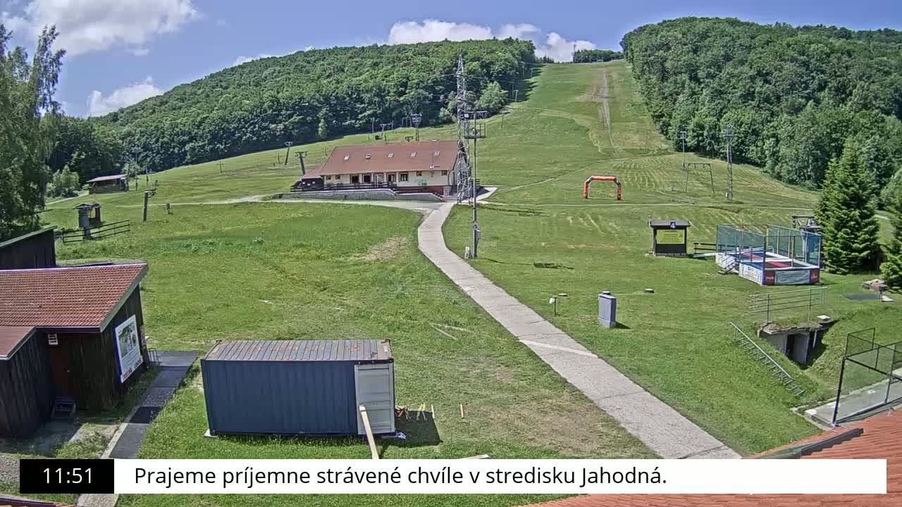 A grassy hillside with a ski lift and small buildings, under a partly cloudy sky.