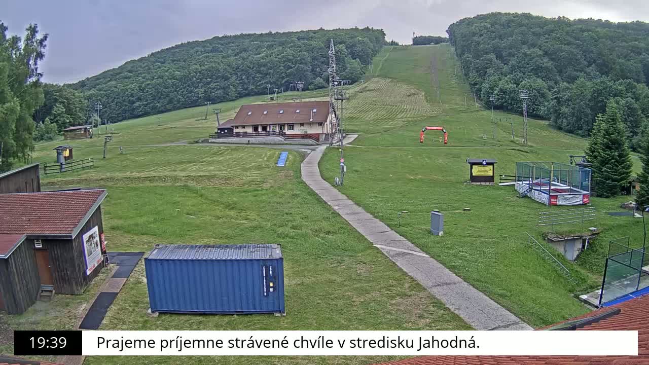 A grassy hillside with a ski lift, buildings, and a paved pathway under an overcast sky.