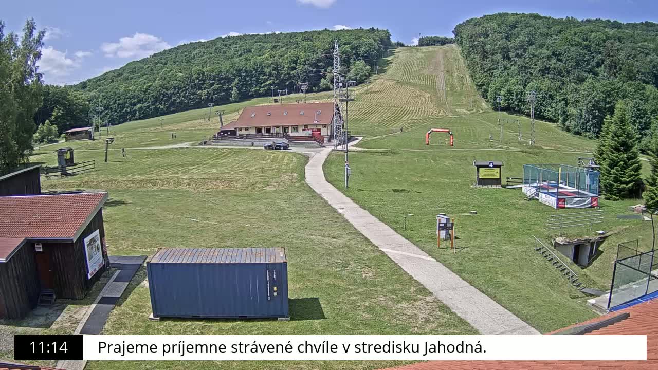 A sunny day at a grassy ski resort with a small building, a paved path, and a trampoline.