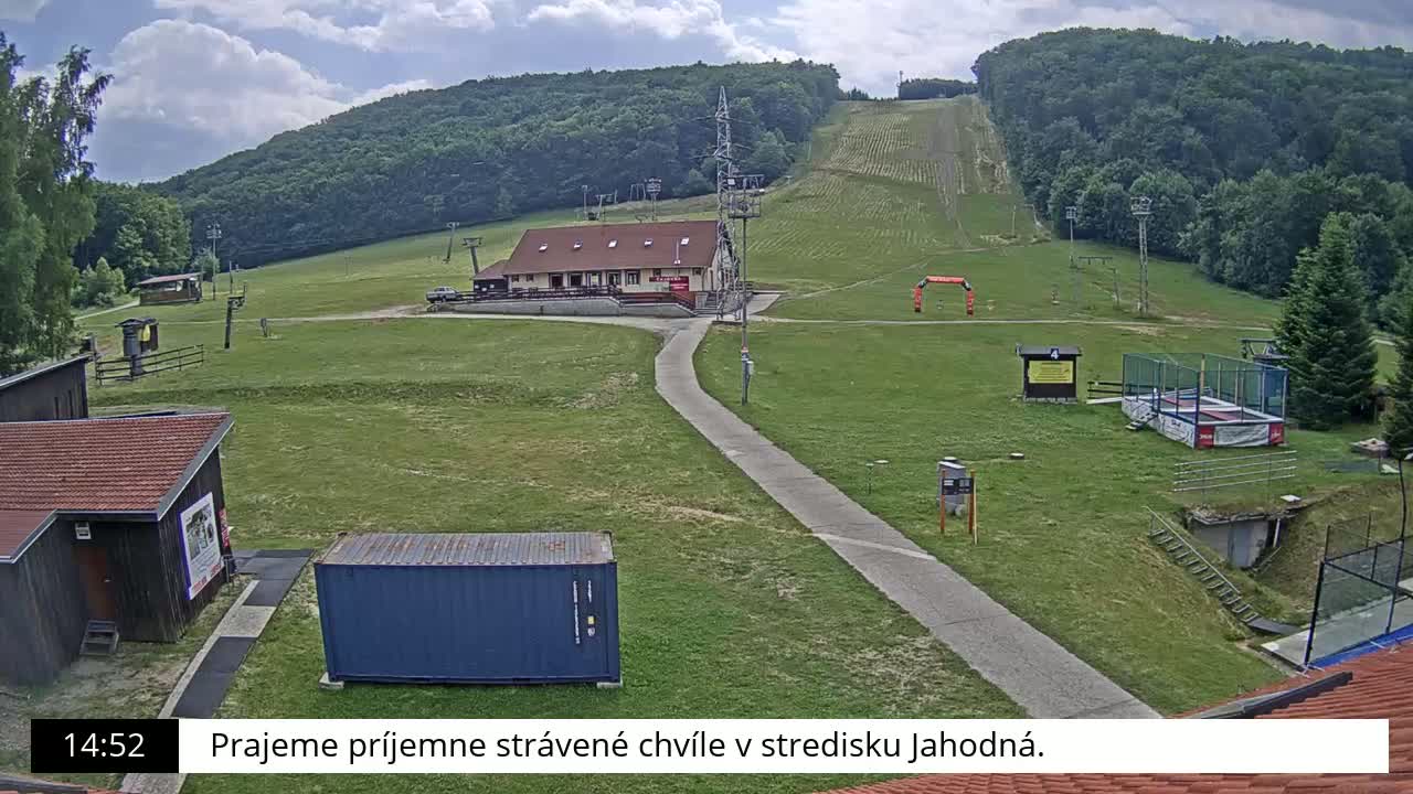 A grassy hillside with a ski lift and a small building, under partly cloudy skies.