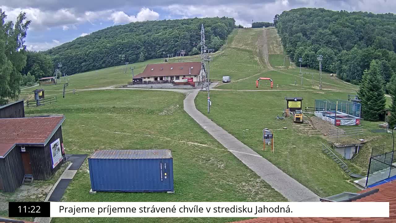 A ski slope with a building, grassy areas, and overcast skies is visible.