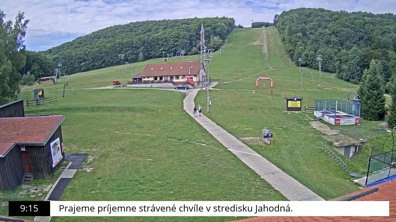 A ski slope with a building and other structures is visible on a partly cloudy day.