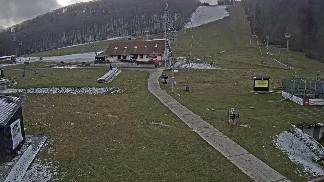 A ski slope with a building and other structures is visible on a partly cloudy day.