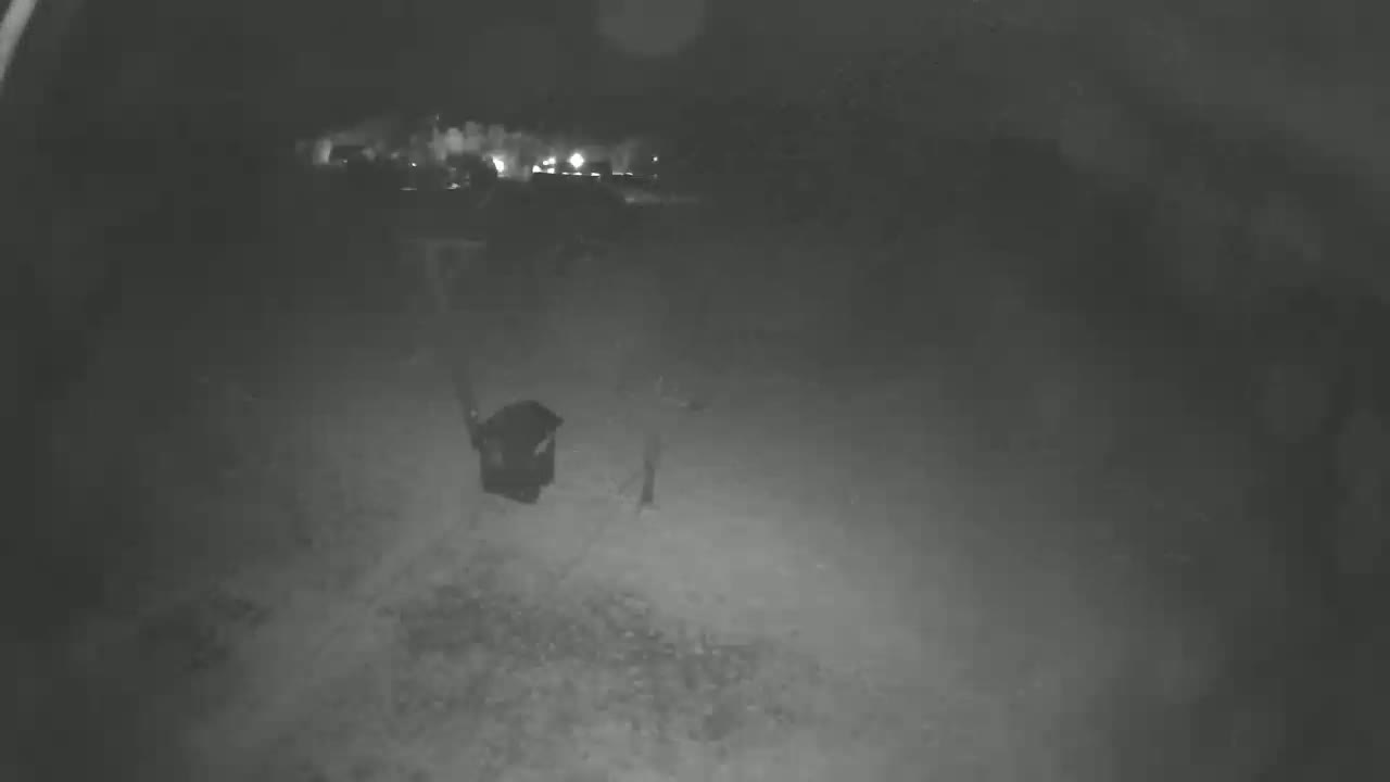 A person carries a dark object at night in a dimly lit area.
