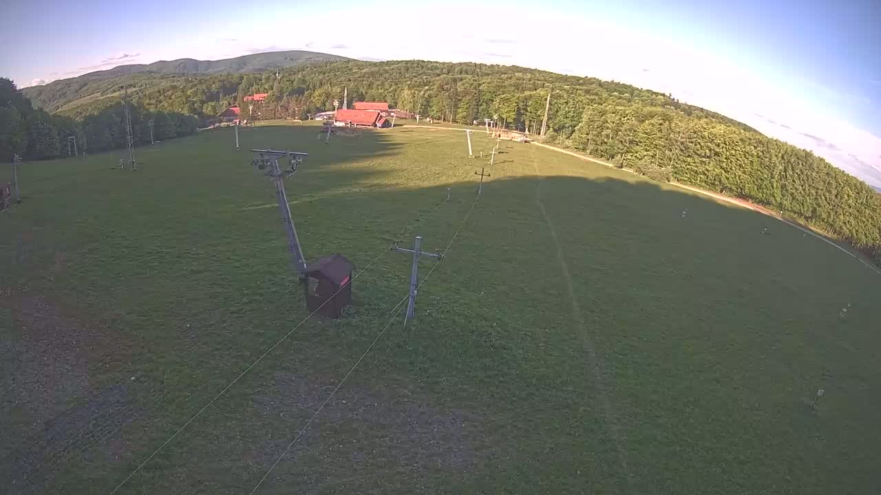 A grassy field with a ski lift and a building in the distance under a clear, sunny sky.