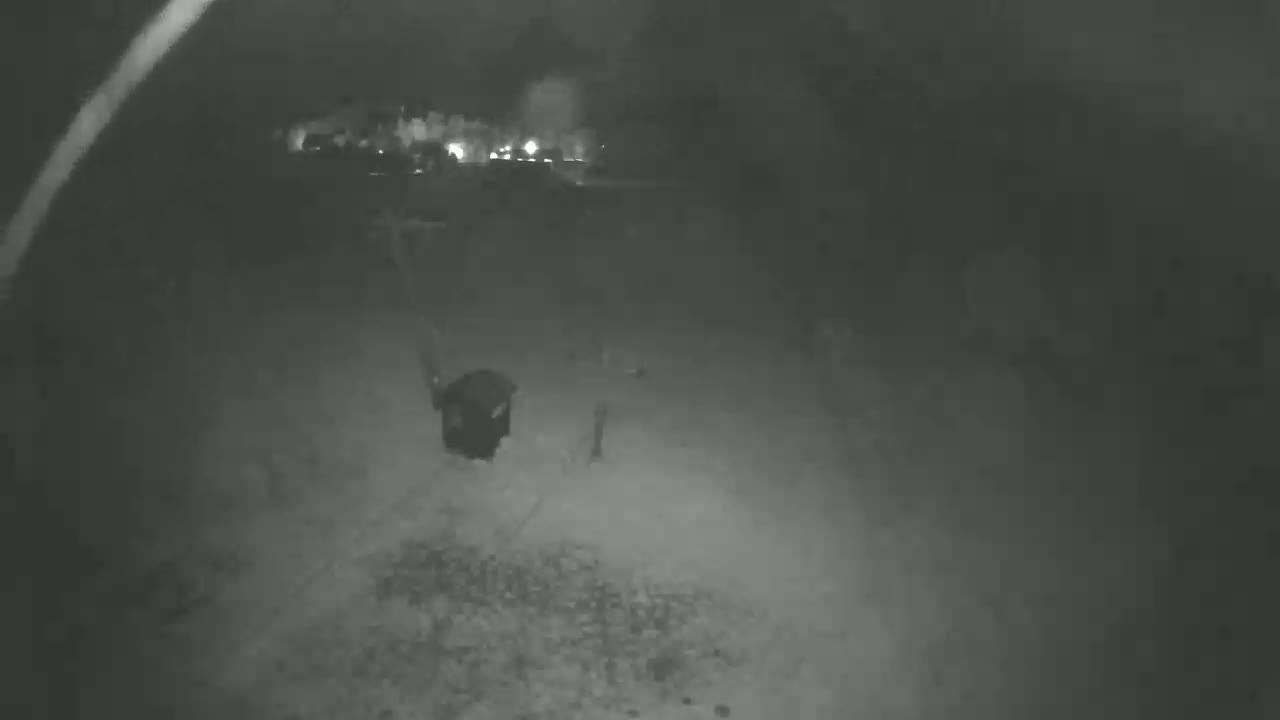A grainy, low-light image shows a dark figure walking on a gravel path at night.