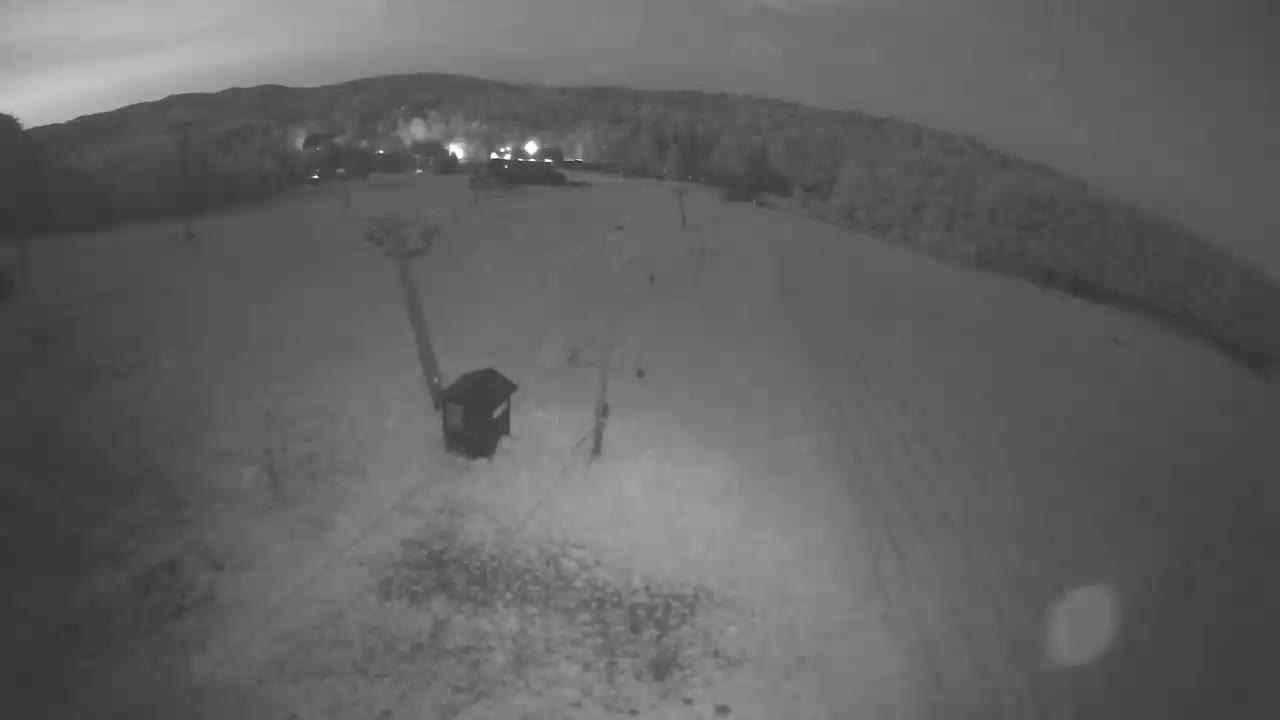 A nighttime, snow-covered ground is shown with a small structure and a distant hill under a dark sky.