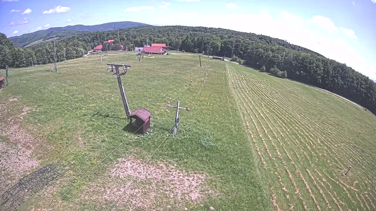 A grassy hillside with a ski lift infrastructure, a few buildings, and a partly cloudy sky.