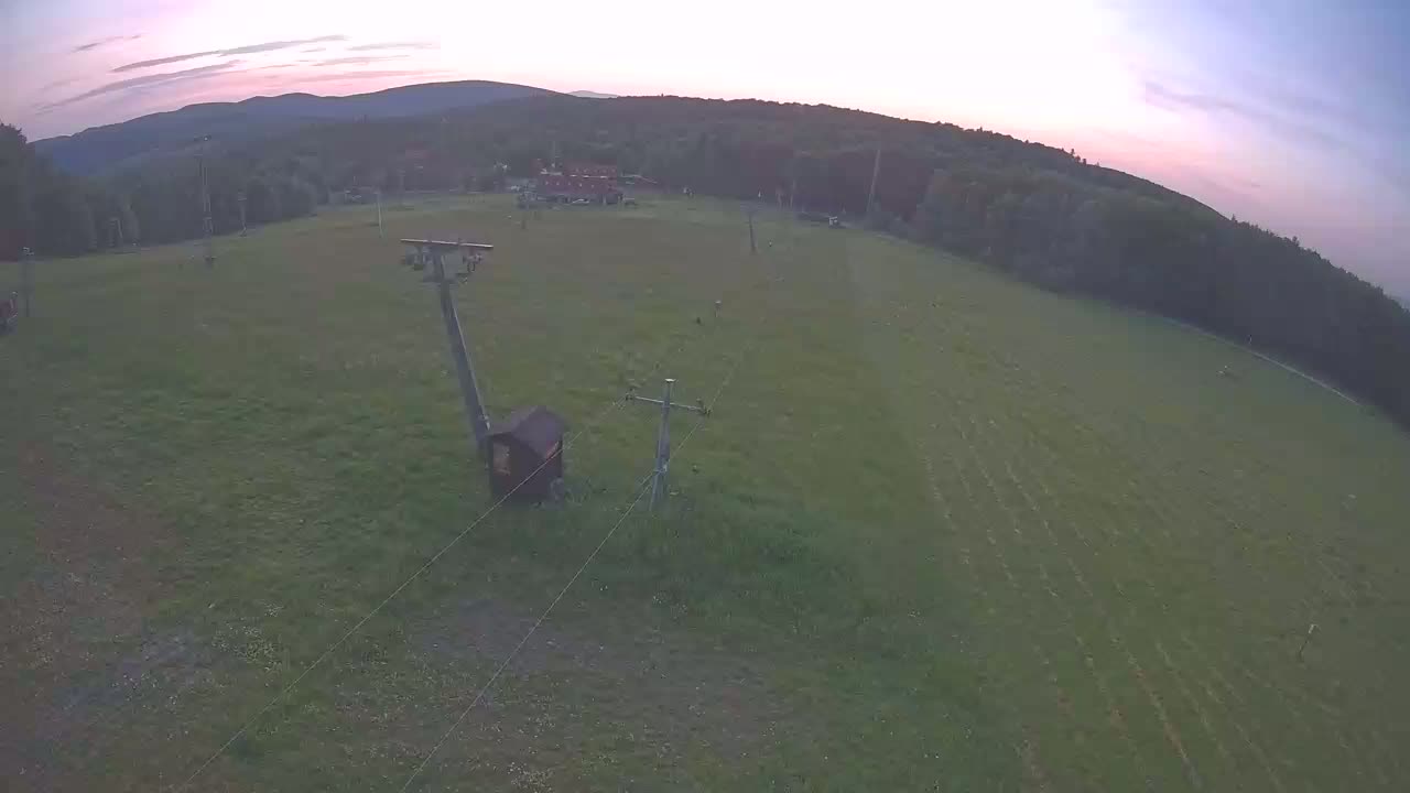 An aerial view shows a grassy field with two utility poles and a small wooden structure under a twilight sky.