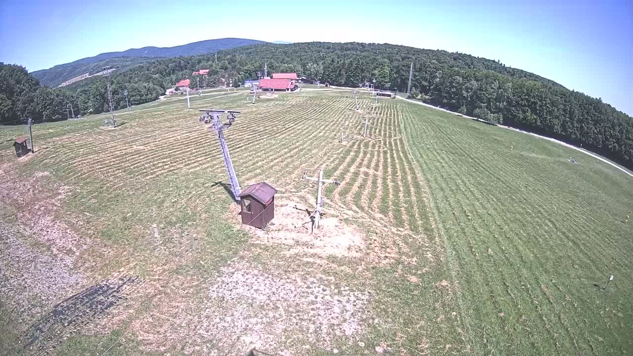 A grassy hill with a ski lift and small buildings is visible under a clear, sunny sky.