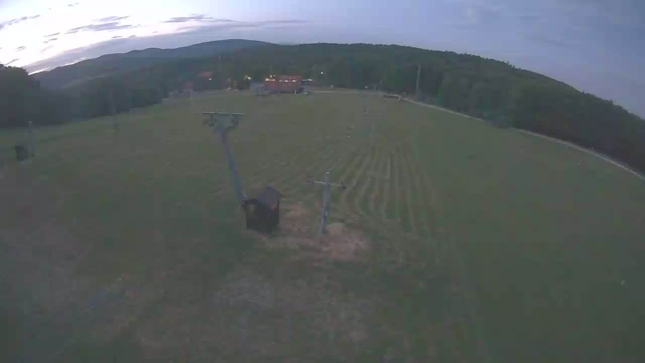 An aerial view shows a grassy field with a ski lift and small building under a twilight sky.