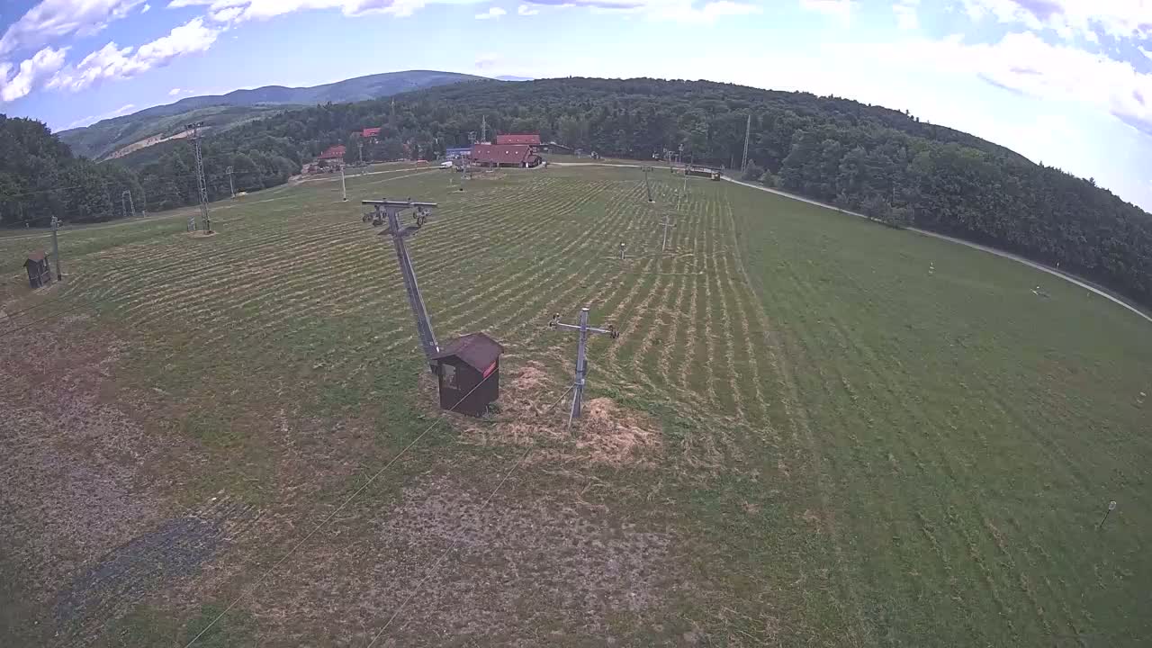 An aerial view shows a grassy field with a ski lift and small building under a twilight sky.