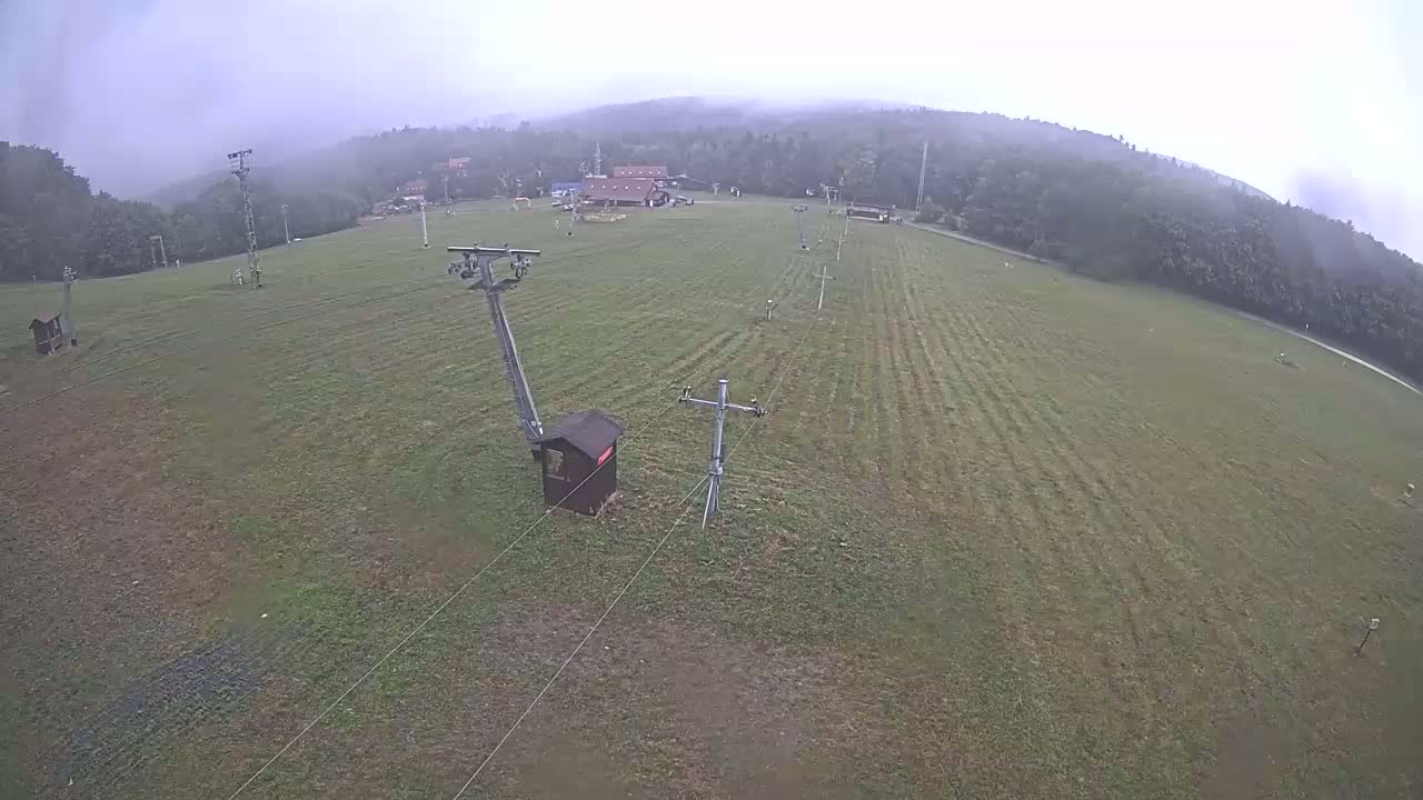 A grassy ski slope with a chairlift and support structures is visible under an overcast sky.