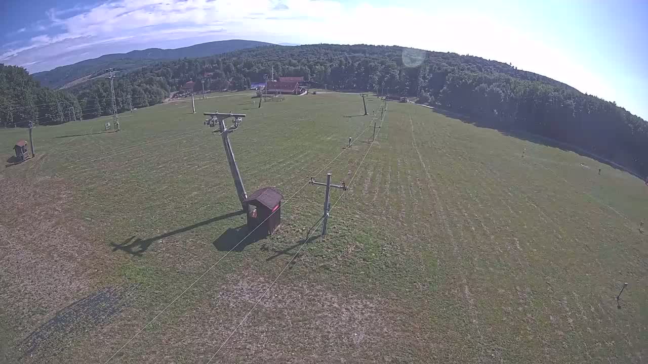 A grassy field with a chairlift infrastructure and a small building, under a partly cloudy sky.