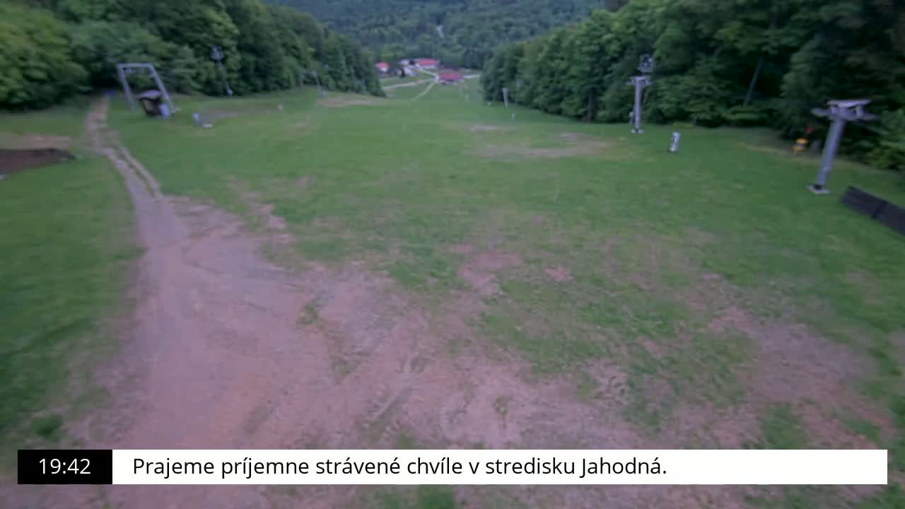 A grassy hill with a dirt path, ski lifts, and a forested background is visible in the evening.