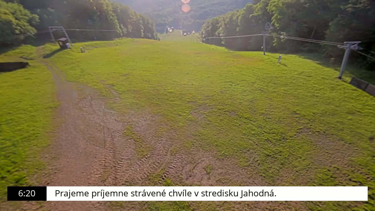 A grassy hillside with a dirt path and chairlift infrastructure is visible on a sunny day.