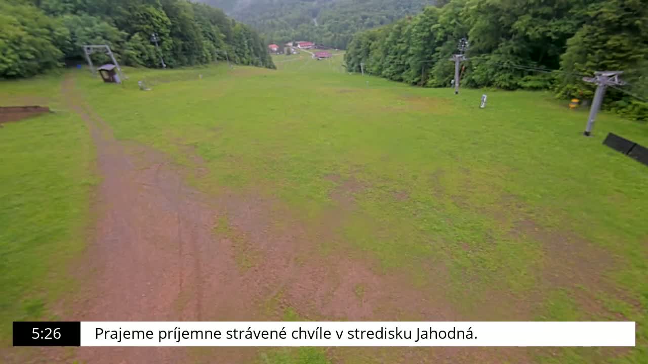 A grassy hillside slopes downward toward a cluster of buildings, with a dirt path and inactive chairlifts visible.
