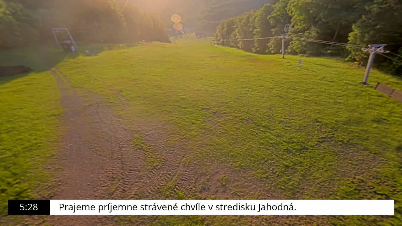 A grassy field with tire tracks and a chairlift in the background, bathed in the warm light of a setting sun.