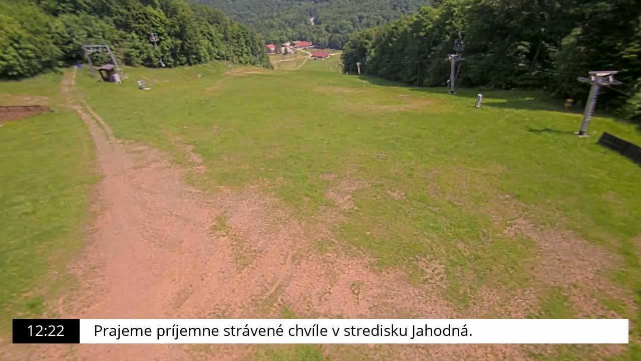 A grassy ski slope with a dirt path and ski lift infrastructure is visible on a sunny day.