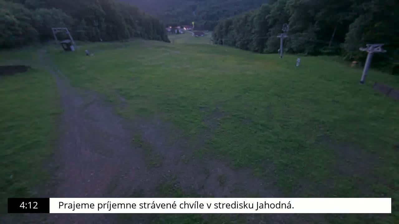 A grassy area with two ski lift supports is visible at dusk, under a dark sky.