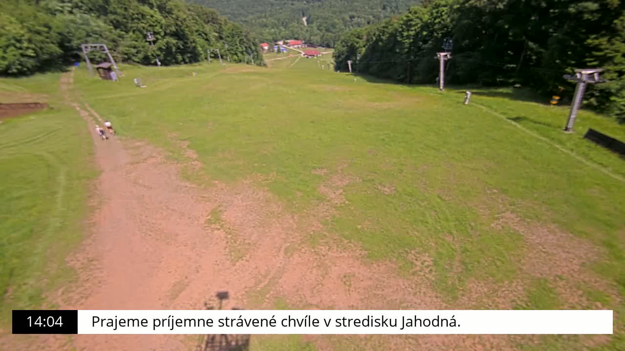 A grassy hill with a dirt path, three people walking, and ski lift infrastructure is visible on a sunny day.