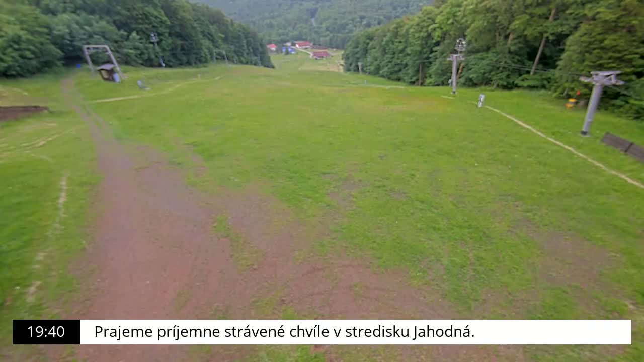 A grassy ski slope with two chairlifts is visible, surrounded by a lush green forest.