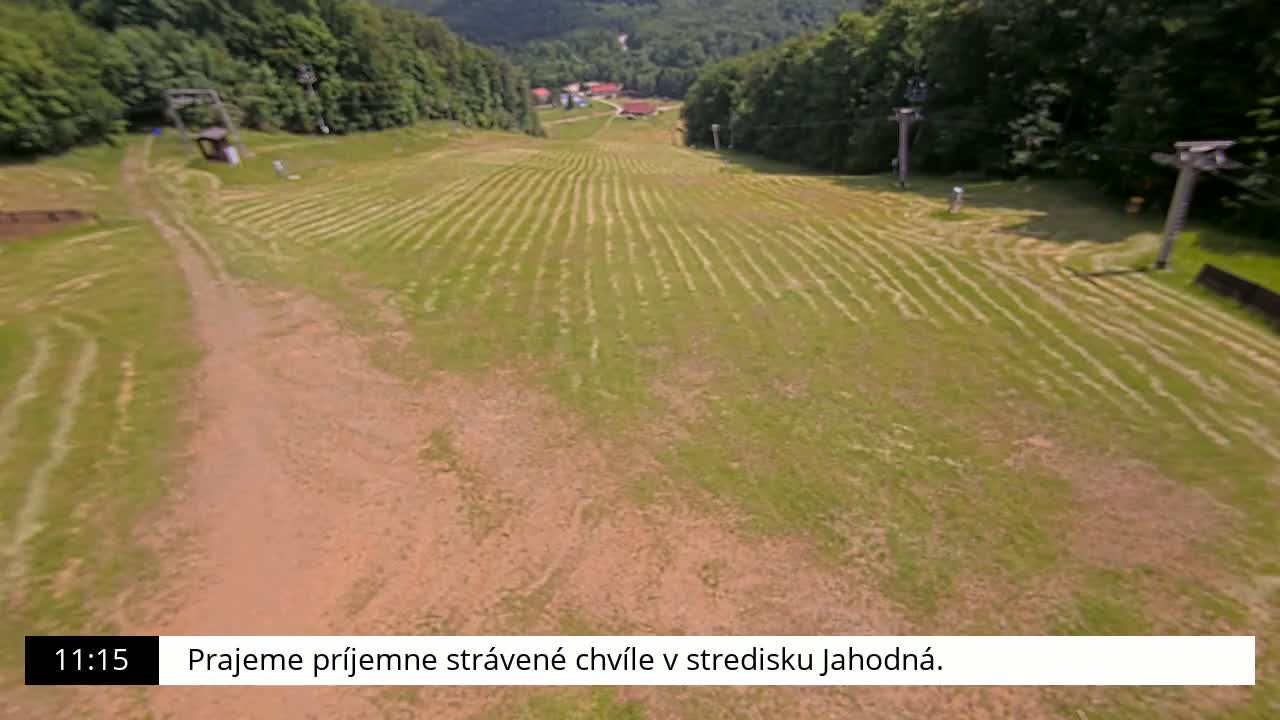 A mown grassy hill slopes downward toward a dirt path, with ski lifts visible in the background under a sunny sky.