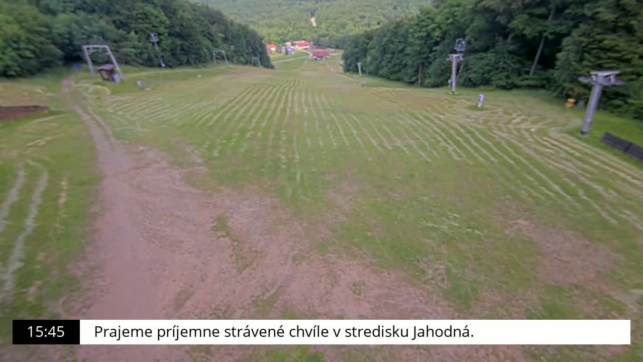 A grassy hill with tire tracks and inactive ski lift infrastructure is visible on a partly sunny day.