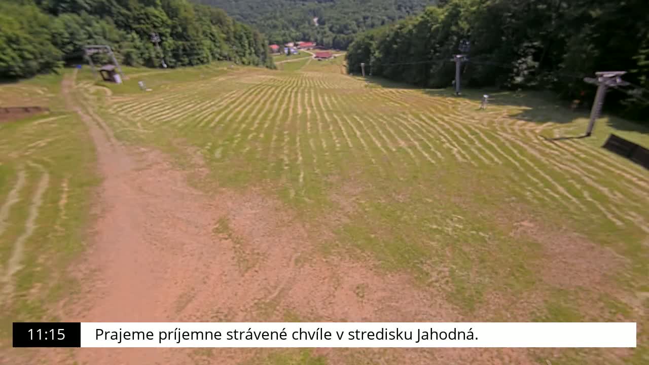 A grassy hill with parallel lines cut into the grass, a dirt path, and two chairlifts is visible on a sunny day.