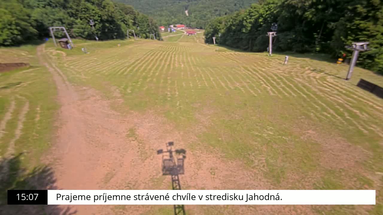 A grassy ski slope with a dirt path and the shadows of ski lifts cast on the ground under a sunny sky.