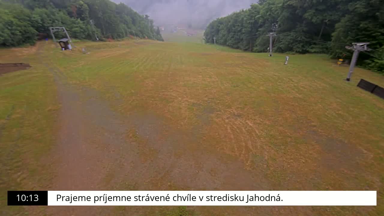 A grassy, mostly brown hill with tire tracks and a chairlift is visible on an overcast day.