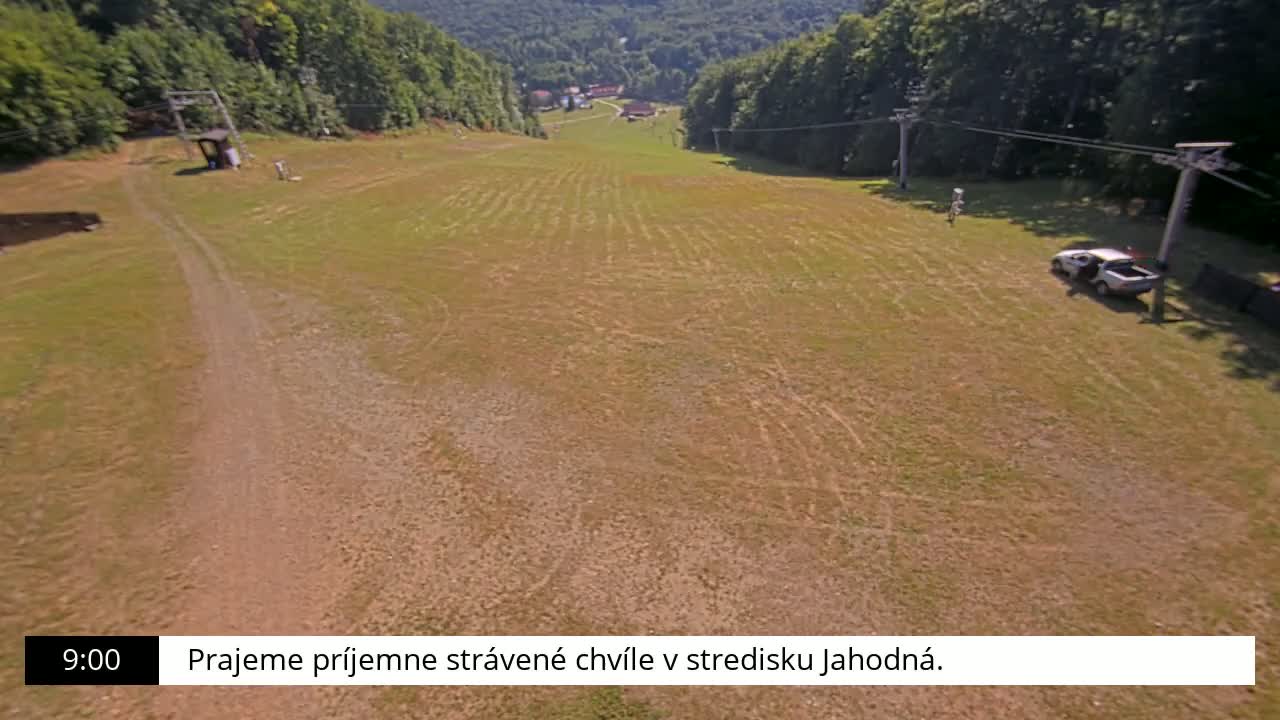 An aerial view shows a grassy field with tire tracks, a dirt road, a ski lift, and a vehicle parked near a ski lift.