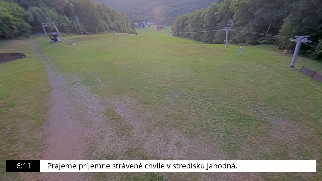 An aerial view shows a grassy field with tire tracks, a dirt road, a ski lift, and a vehicle parked near a ski lift.