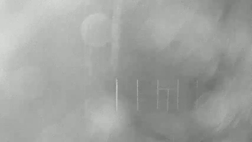A blurry, gray image shows indistinct shapes and faint vertical lines in a foggy or hazy atmosphere.