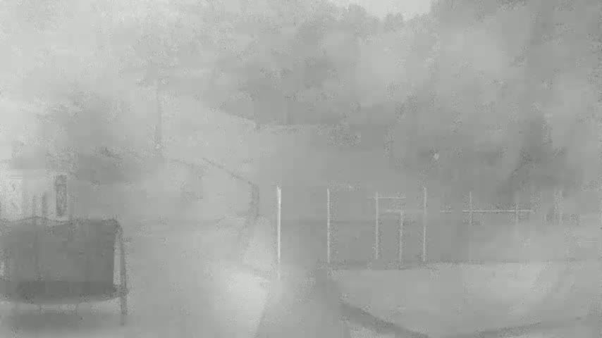 A hazy, foggy outdoor scene shows a section of a fence, parts of buildings, and a piece of furniture.