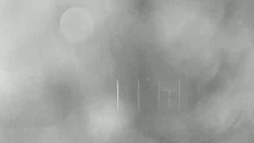 A blurry, hazy view of a structure with vertical lines, possibly a building or fence, is seen through a foggy or misty atmosphere.