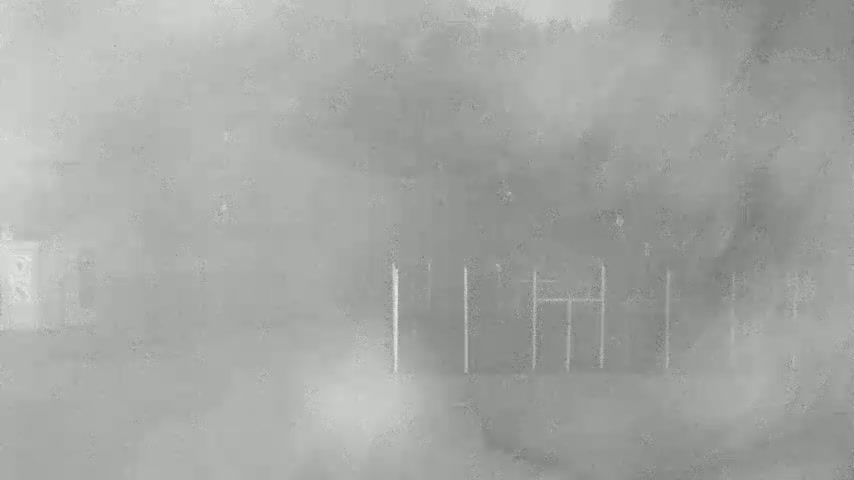 A foggy or hazy outdoor scene shows indistinct structures, possibly trees and a partially visible metal framework, in the mid-ground.