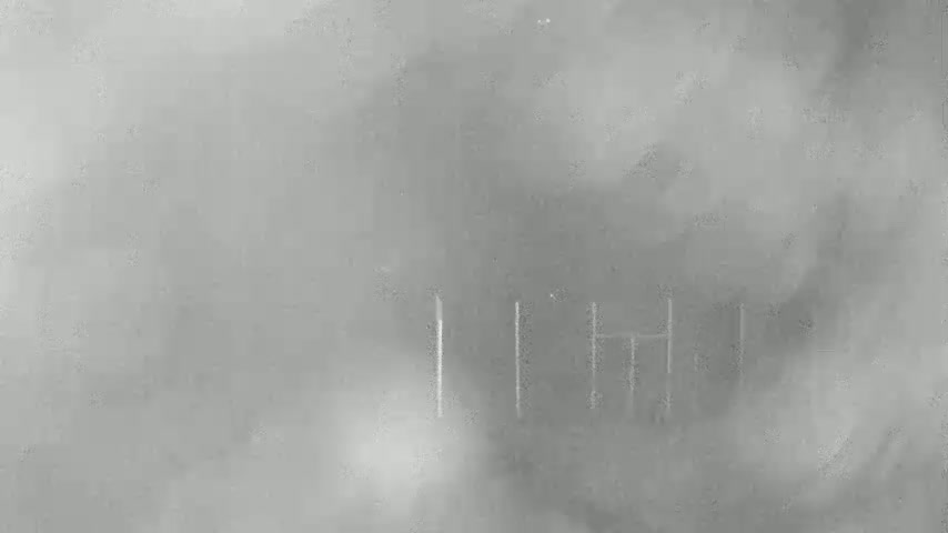 A foggy or hazy scene shows faint vertical lines suggesting a structure or fence in the distance.