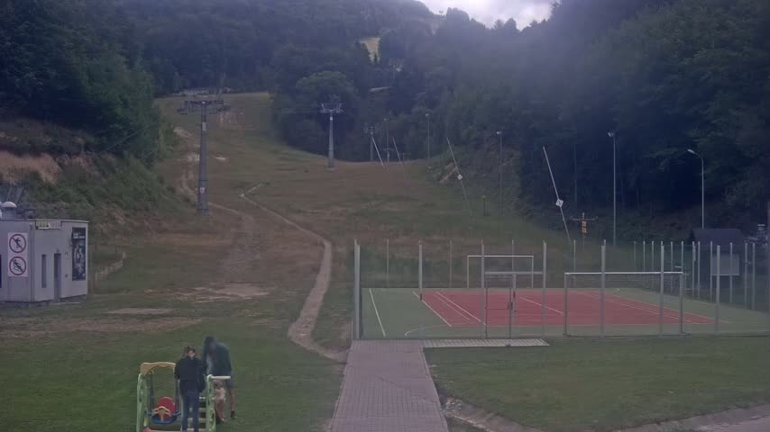 A hillside ski lift, a multi-purpose sports court, and a small playground are visible on an overcast day.
