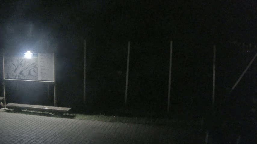 A lit sign with a map and a bench are in front of a dark fence at night.