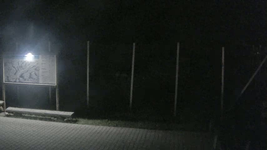 A dimly lit nighttime scene shows a map on a post, a bench, and a dark fence behind it.