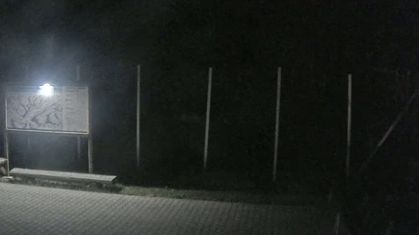 A nighttime scene shows a lit-up map and a bench in front of a dark fence.