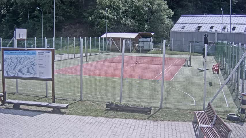 An outdoor tennis court and basketball court are enclosed by a chain-link fence on a sunny day.