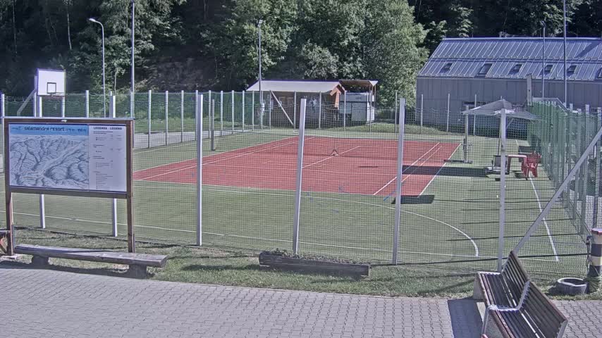 An outdoor tennis court, enclosed by a chain-link fence, sits next to a basketball court on a sunny day.