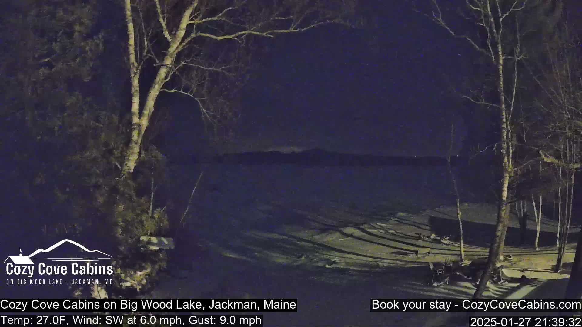 A nighttime view of a snow-covered lakeshore with bare trees under a dark sky, with a southwest wind at 6 mph and gusts up to 9 mph.