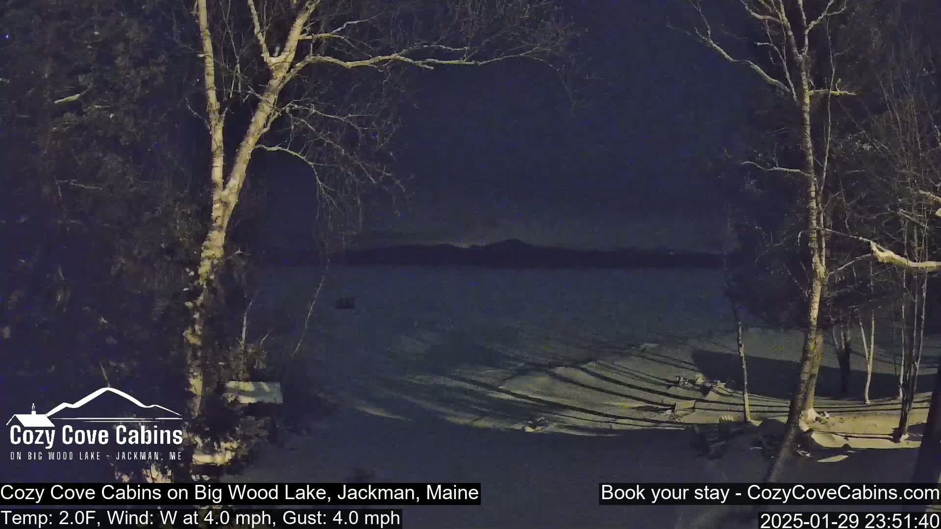 A nighttime view of a snow-covered lakeshore with leafless trees under a dark sky, a 2°F temperature, and a westerly wind of 4 mph with gusts up to 4 mph.